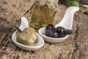 Green and black olives and olive oil on wooden table